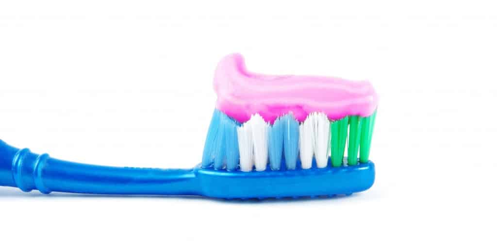 Line of pink toothpaste on the bristles of a blue toothbrush
