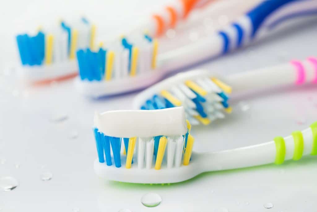 Four multi-colored toothbrushes with toothpaste.