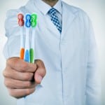 Dentist holding three multicolored toothbrushes